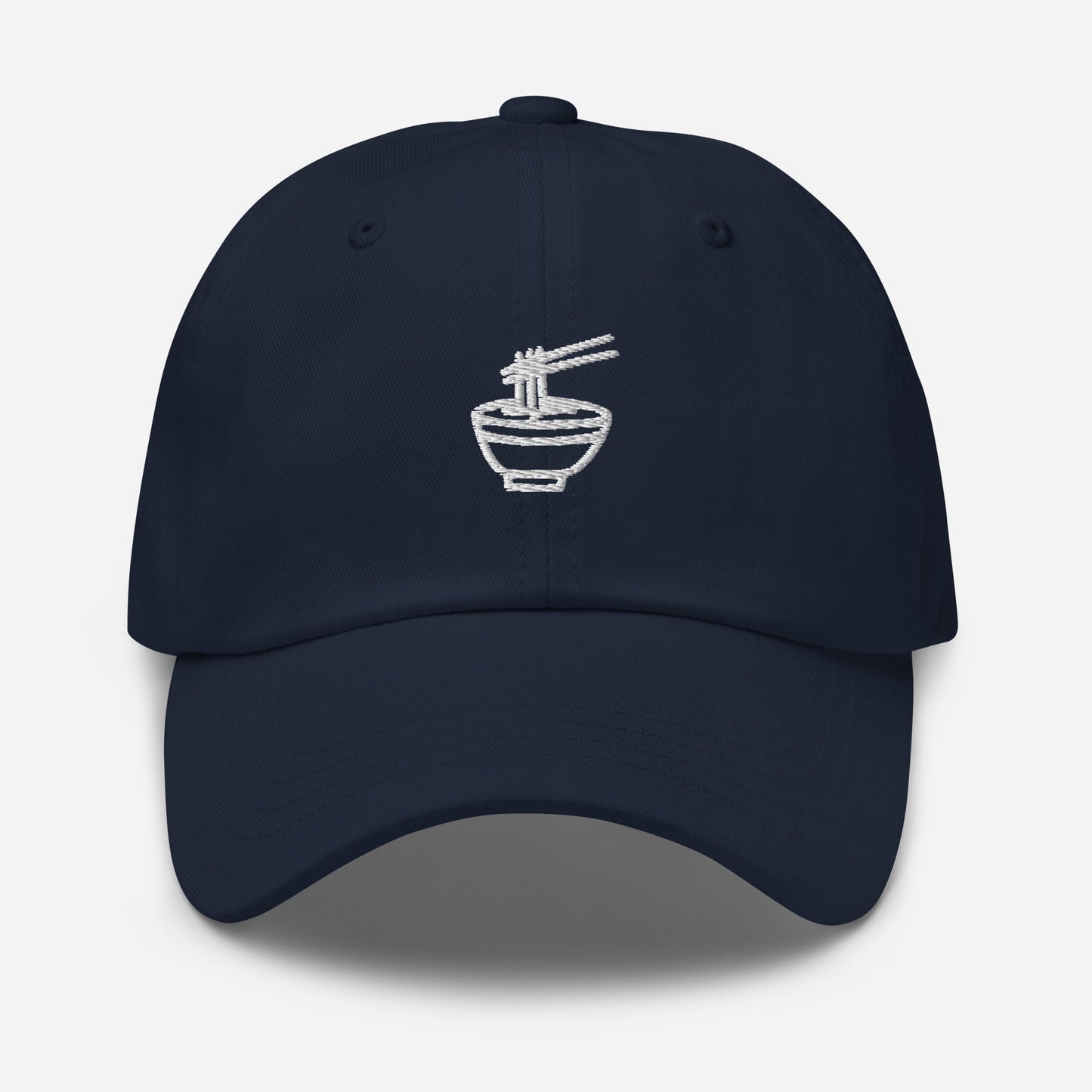 Navy blue dad hat with white emblem stitching of a noodle bowl with chopsticks picking up noodles in the middle of the front of the hat. Front View