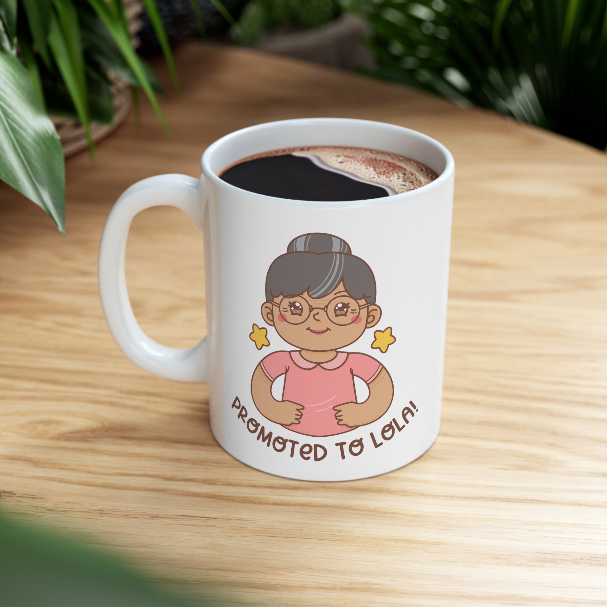 White mug with a kawaii picture of an old woman in a pink shirt wearing glasses. A caption below the picture reads Promoted to Lola! Front view