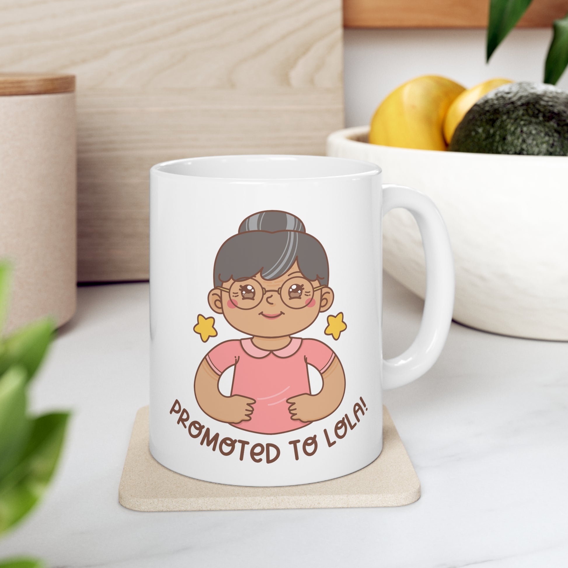 White mug with a kawaii picture of an old woman in a pink shirt wearing glasses. A caption below the picture reads Promoted to Lola! Front view