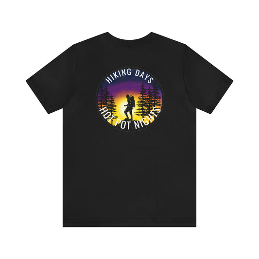 Black t-shirt of a hiker in the woods during sunset with a purple and gold sky all enclosed in a circle. The words Hiking Days at the top of the circle and Hot Pot Nights at the bottom of the circle. Front view.